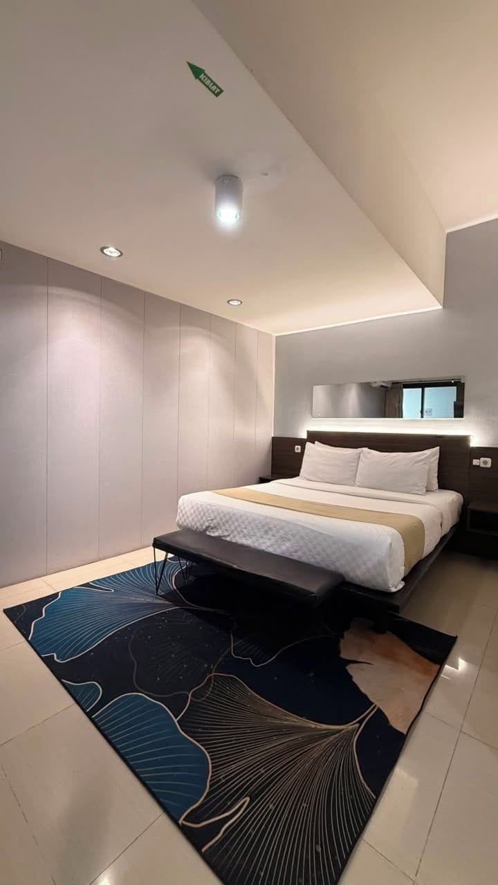 Un dormitorio moderno con una cama, mesitas de noche, un banco, una lámpara de techo y un espejo de pared.