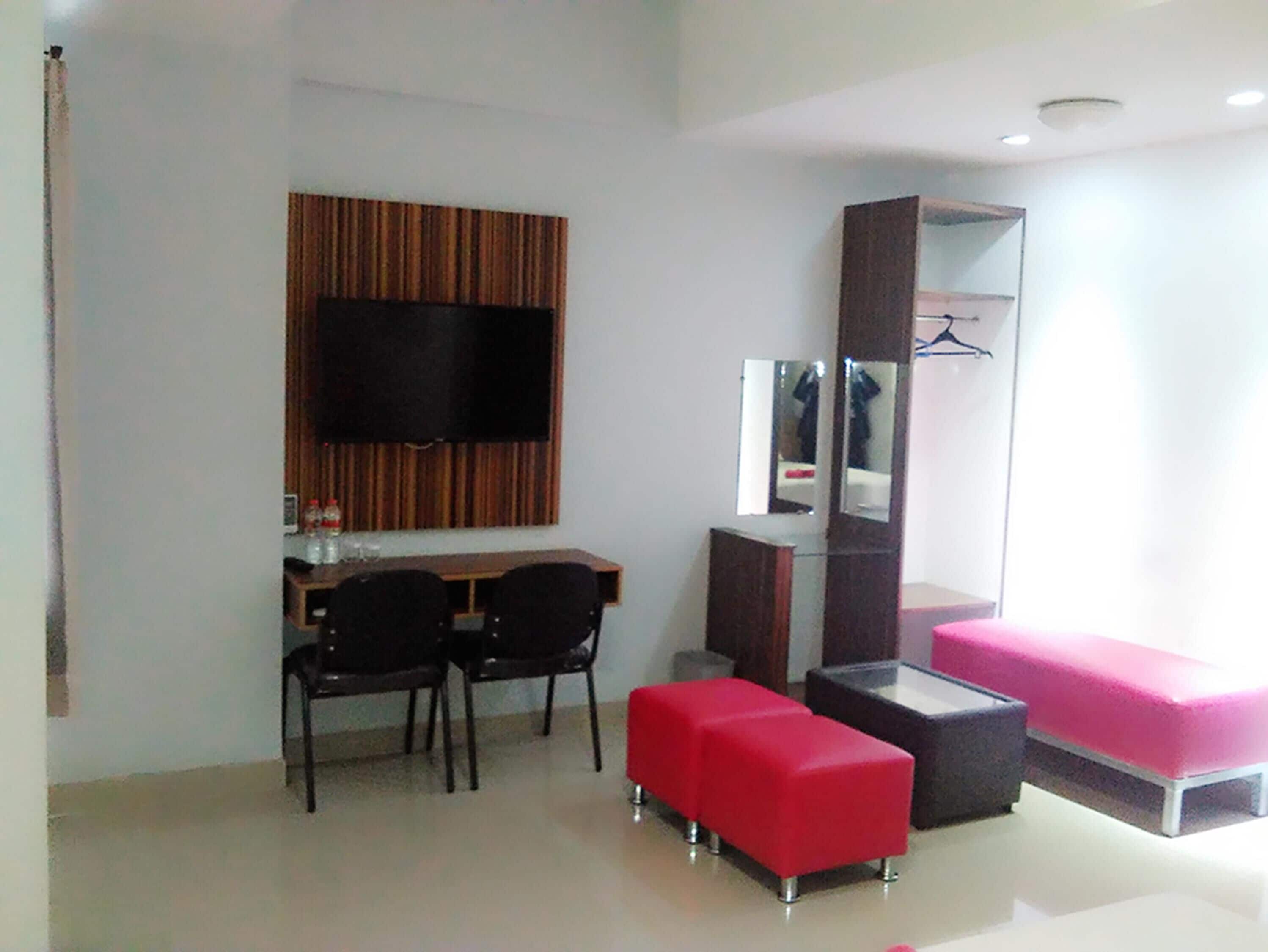 A modern room with a flat-screen TV, a wooden panel wall, a mirror, a red sofa, and a small table with two chairs.