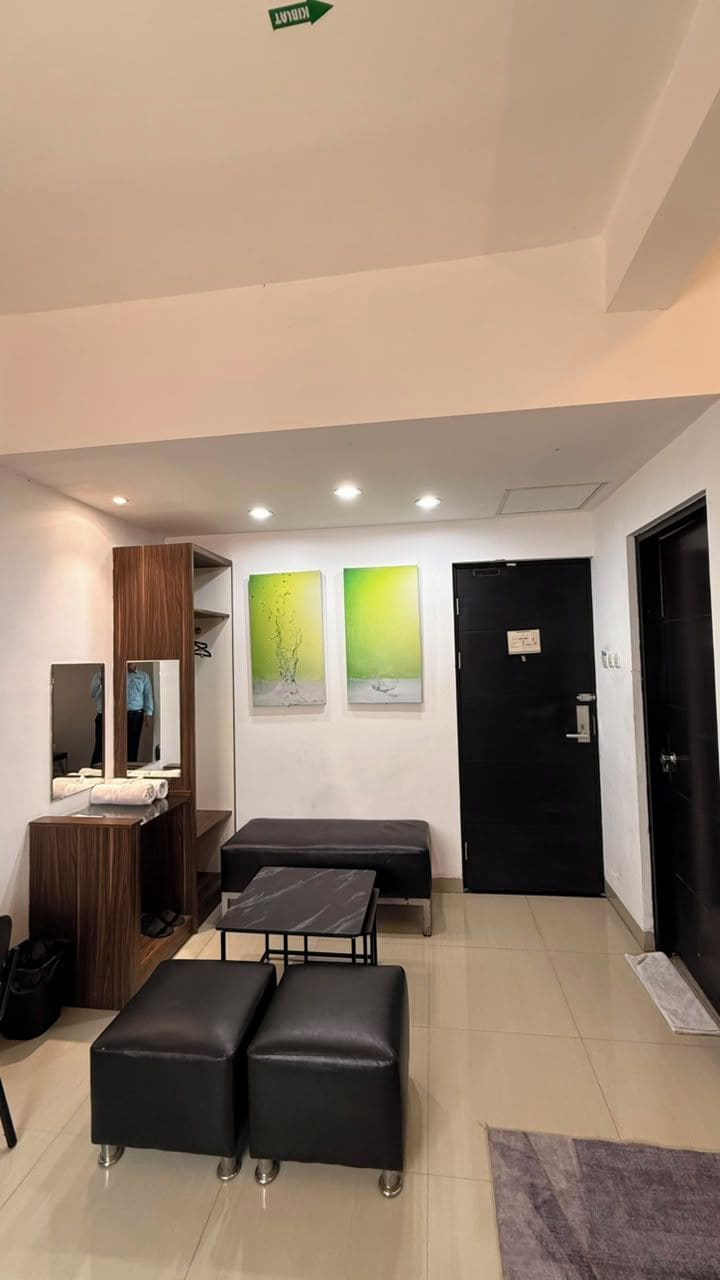 Una habitación con una puerta negra, un banco, dos otomanas, un espejo y obras de arte en la pared.