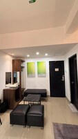 Una habitación con una puerta negra, un banco, dos otomanas, un espejo y obras de arte en la pared.