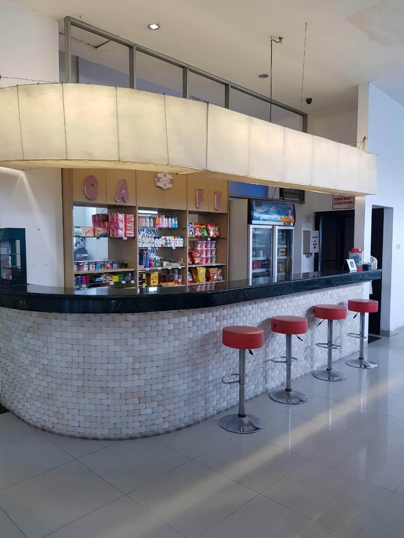 Eine Bar mit einer gefliesten Theke, Regalen voller Snacks und drei roten Barhocker.