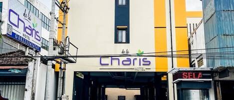 A hotel with a yellow and white facade, a visible entrance, and a car parked in front.