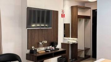 Habitación de hotel con cama, escritorio con televisor de pantalla plana, espejo, armario y zona de estar.