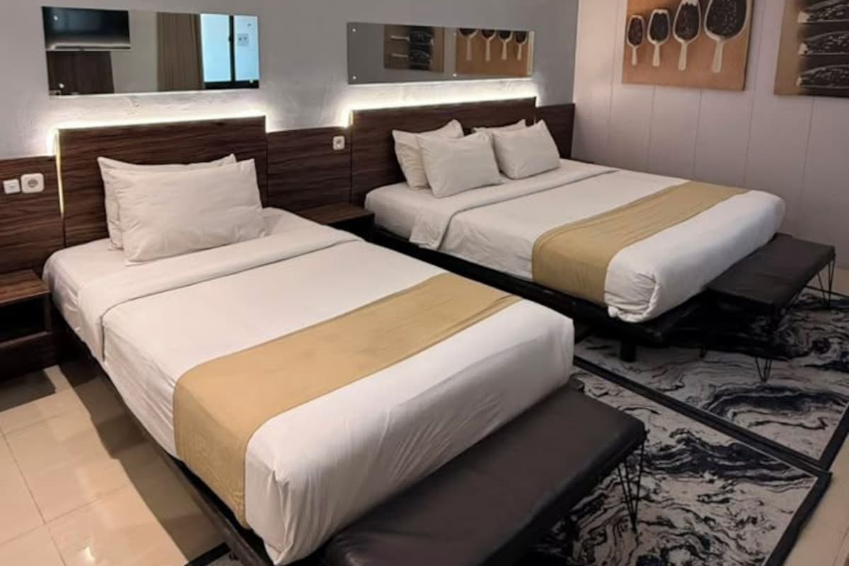A hotel room with two beds, a bench, a marble-patterned rug, and a ceiling light.