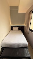 Una habitación pequeña con cama individual, cabecero, mesita de noche y ventana con cortinas.