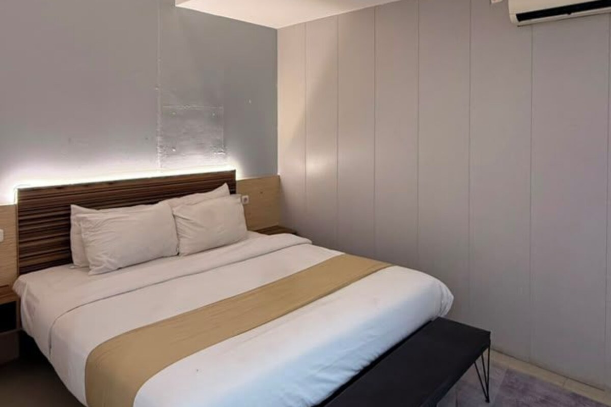 A modern bedroom with a bed, bench, and an air conditioning unit.