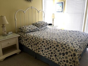 Um quarto com cama, mesa de cabeceira, luminária e janela com persianas.