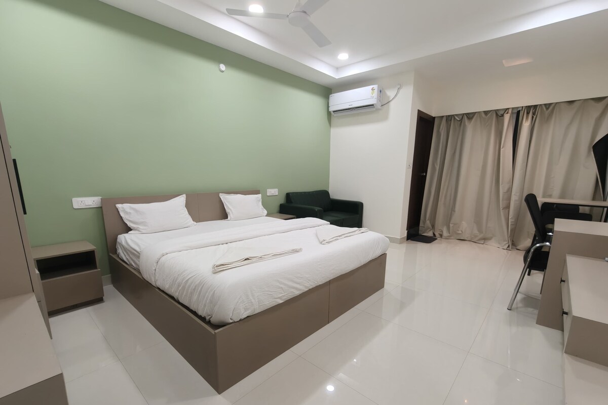 Quarto de hotel moderno com uma cama grande, uma escrivaninha, uma cadeira e uma parede verde.
