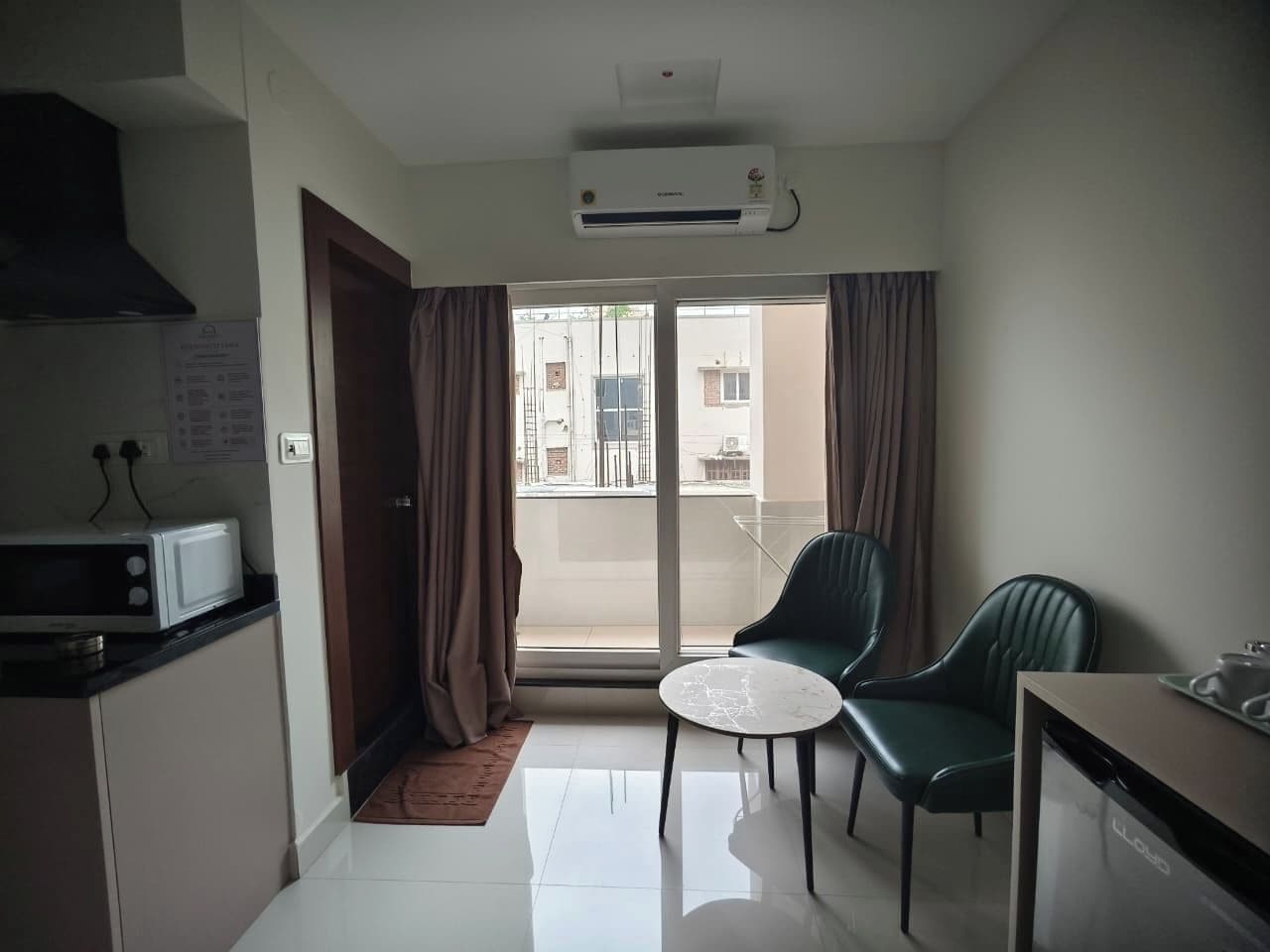 Un espacio habitable compacto con kitchenette, una zona de comedor con dos sillas, una mesita redonda y un ventanal corredizo que da a un balcón.