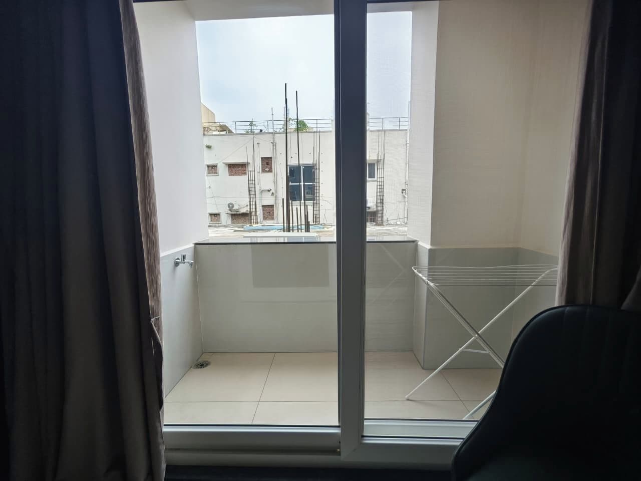 Un balcón con barandilla de metal, una silla y vistas a edificios al fondo.