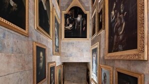 Un pasillo con retratos enmarcados en las paredes, piso de mármol y una escalera que conduce a un nivel superior.