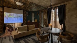 Una habitación acogedora con pared de ladrillo, una pantalla de proyector, un sofá, una mesa de comedor con sillas y una araña.