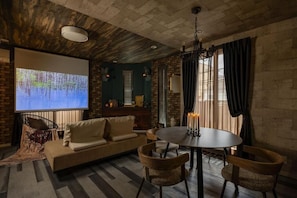A cozy room with a brick wall, a projector screen, a sofa, a dining table with chairs, and a chandelier. - JAPAVISTA Enchant (NISHIKUJŌ, KONOHANA WARD)