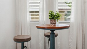 Ein kleiner runder Tisch mit einem Blumentopf, zwei Hocker und einem Fenster mit Jalousien.