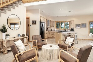 A spacious living area with a round coffee table, several armchairs, a wooden dining table, and a kitchen with wooden cabinets and a large window. - Spacious Cabin with Foosball Table and Jacuzzi in Grand Lake, Colorado (Grand Lake)