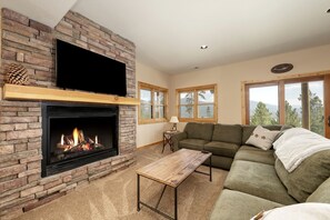 A living room with a fireplace, a television mounted on the wall, a sofa, and a coffee table. - Spacious Cabin with Foosball Table and Jacuzzi in Grand Lake, Colorado (Grand Lake)