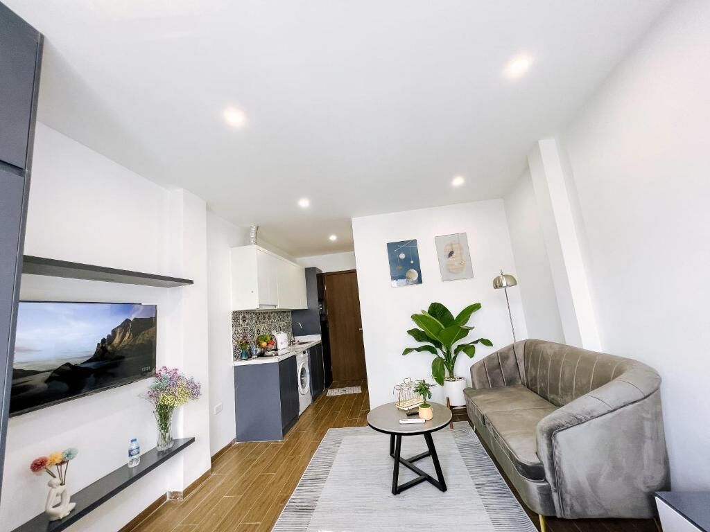 Un salon moderne avec un canapé, un téléviseur, une petite table et une cuisine en arrière-plan.