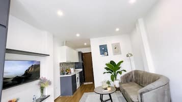 Un salon moderne avec un canapé, un téléviseur, une petite table et une cuisine en arrière-plan.