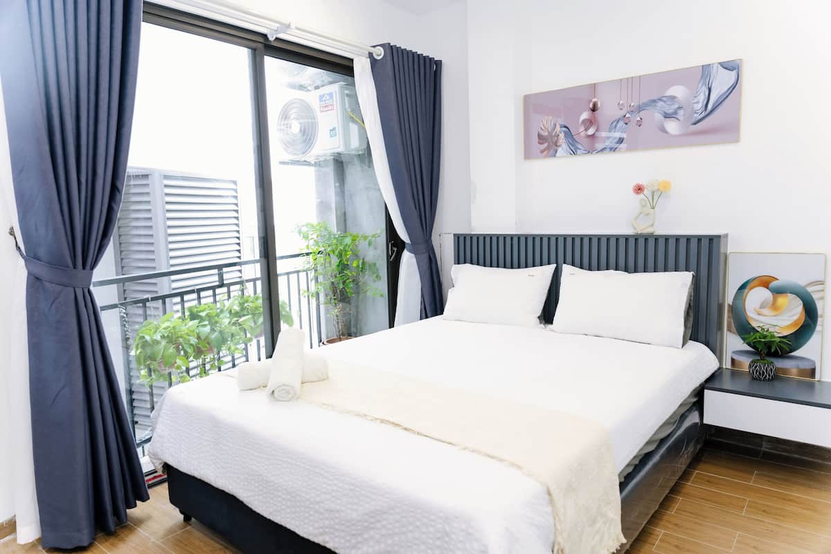 Un dormitorio con cama, mesita de noche, ventana con cortinas, radiador, planta y una obra de arte en la pared.
