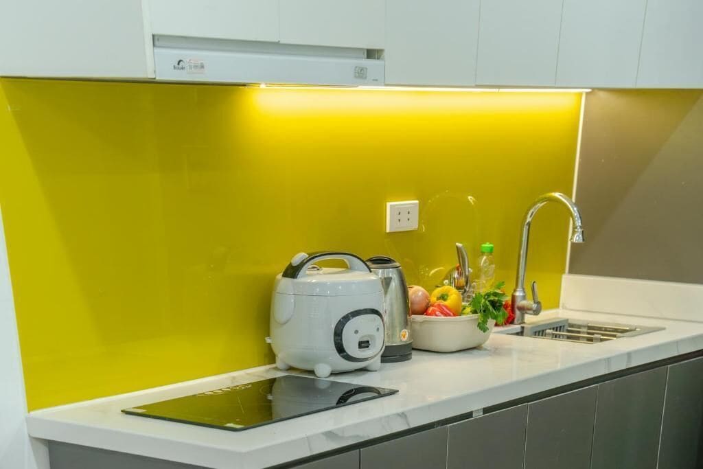 A kitchen with a yellow backsplash, a sink, a kettle, a bowl of fruit, and a tablet on the counter.