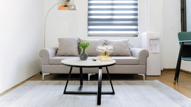En moderne stue med en sofa, et rundt sofabord, en potteplante, en vanddispenser og en gulvlampe.