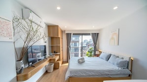 Et moderne hotelværelse med en stor seng, et skrivebord, en stol, et lille bord, en plante og et vindue med udsigt over byen.