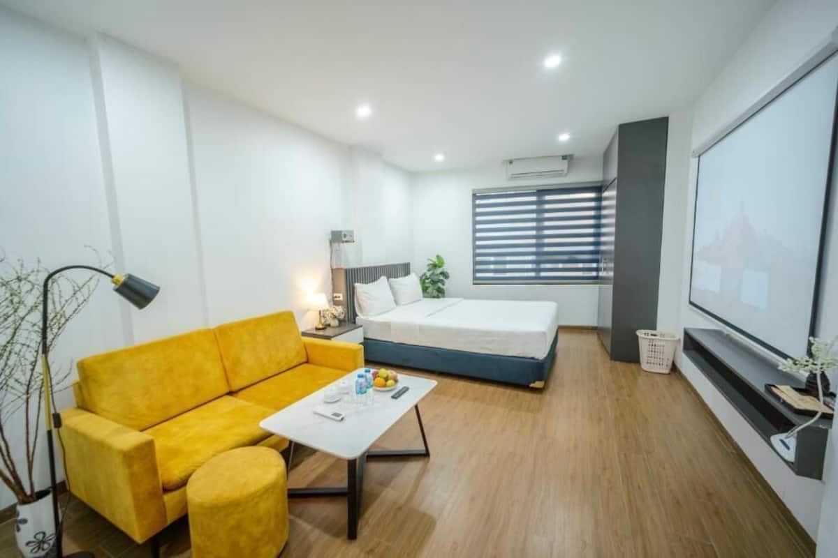 Una habitación moderna con sofá, cama, una mesita, lámpara, televisión y ventana con persianas.