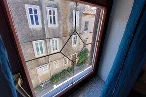 A window with a geometric pattern, a view of a building with multiple windows, and a blue curtain partially visible. - Rooms Argo- Turquoise Double Room (Cres)