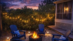 A patio with four Adirondack chairs, a fire pit, and string lights. - Spacious Gulf Shores Beach House with Pool Access and Ocean Views (Gulf Shores)