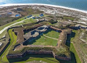 Luftaufnahme einer historischen Festung mit einem Burggraben, umgeben von Grünflächen und einem Strand.