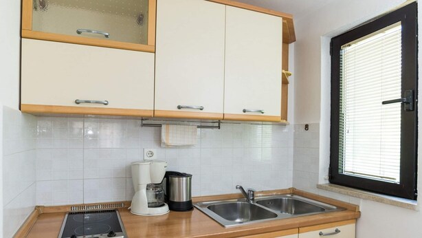 A kitchen with white cabinets, a window with blinds, a stove, a coffee maker, and a sink. - Apartments Alba - 1 Bedroom Apartment (Rovinj)