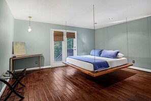 A modern bedroom with a hanging bed, a desk, and a view through a glass door.