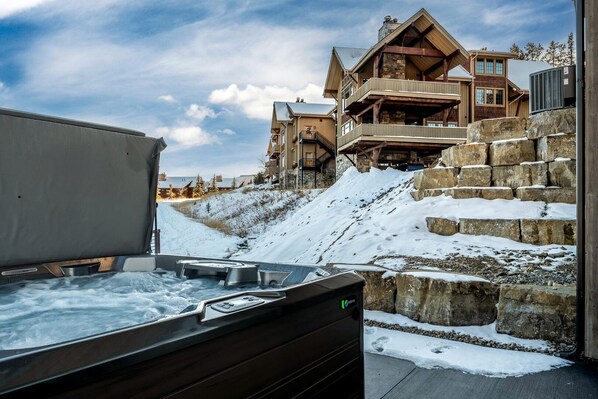 Un bain à remous sur une terrasse, avec vue sur un immeuble à plusieurs étages et des marches recouvertes de neige.