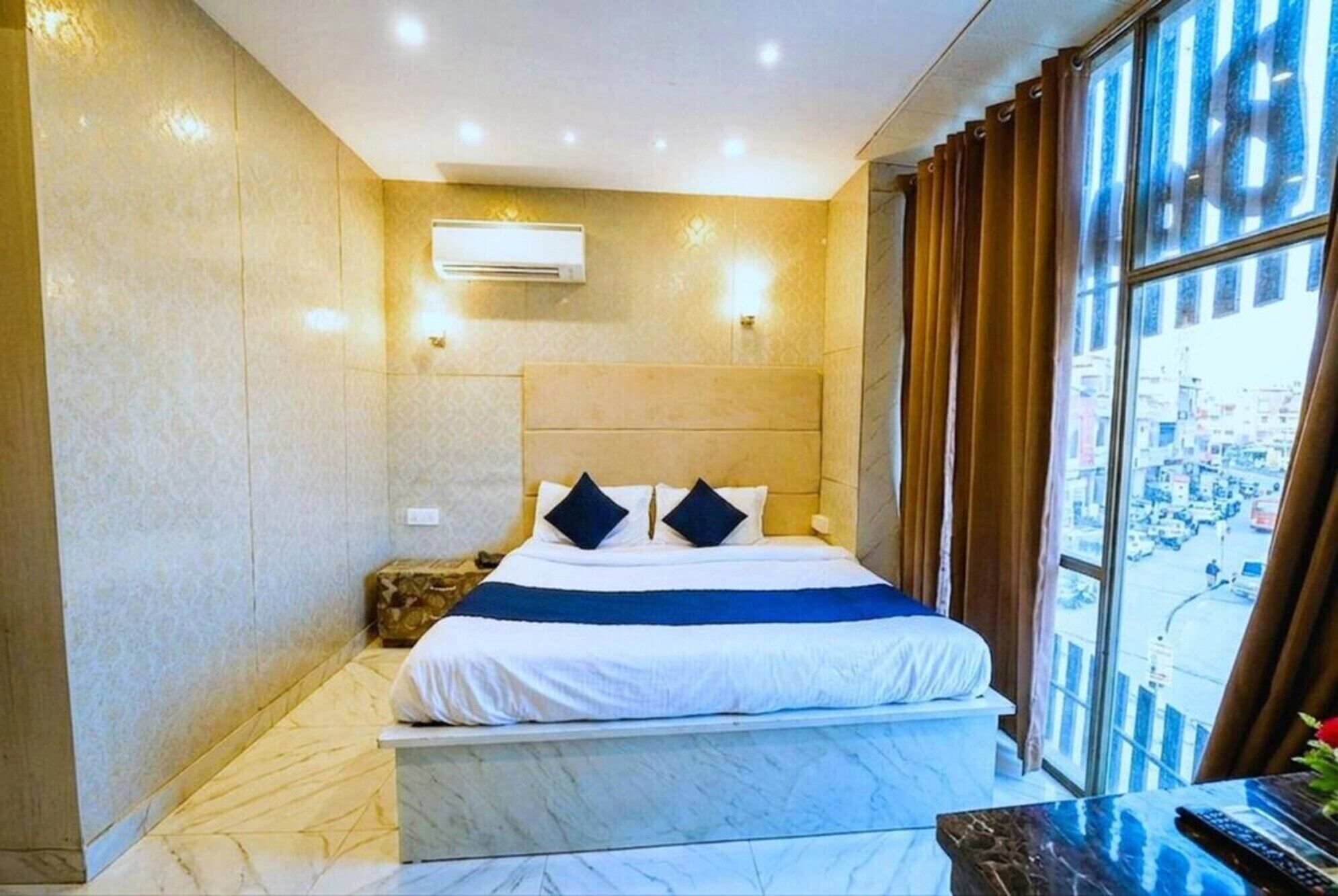 Camera d'albergo con un letto, un comodino, un condizionatore, una finestra con tende e vista sulla città.