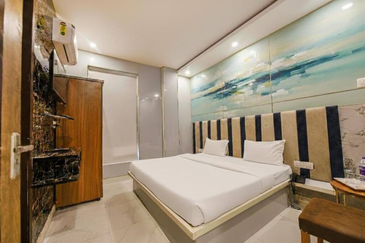 A hotel room with a bed, a wooden wardrobe, a nightstand, and a wall with a painting.