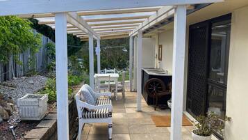 A covered patio area with a white chair, a table, and a potted plant.