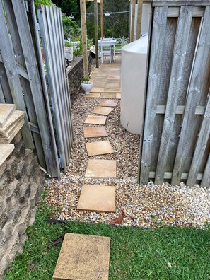 Ein Gartenweg mit trittsteinförmigen Steinen, einem Holzzaun und einer Steinmauer.