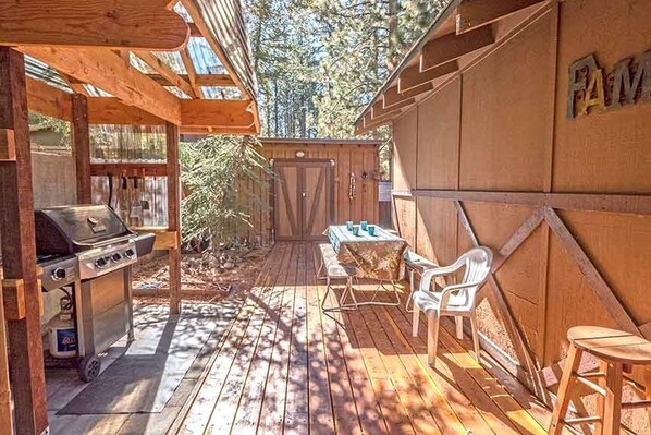 Une terrasse en bois avec un barbecue, une table et des chaises, et un mur en bois sur lequel est inscrit le mot « FAMILLE ».