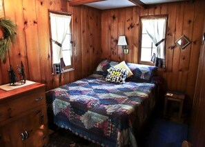 A wooden cabin-style room with a bed, dresser, and two windows. - Fantastic, Cute, Lakefront Cabin in Carp Lake, Michigan (Carp Lake)