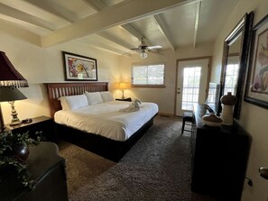 Ein Schlafzimmer mit Bett, Nachttisch, Lampe, Deckenventilator, Fenster und Kommode.