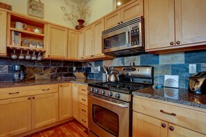 A kitchen with wooden cabinets, a stainless steel stove, a microwave, and a granite countertop.