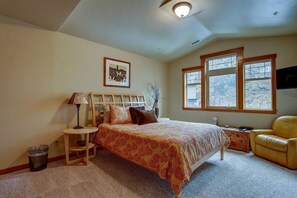 A bedroom with a bed, bedside table, lamp, chair, and a window with a view.