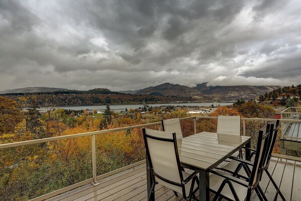 A deck with a table and chairs overlooking a lake and mountains.