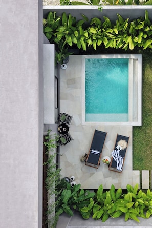 Uma piscina no terraço com espreguiçadeiras, uma mesa e plantas em vasos.