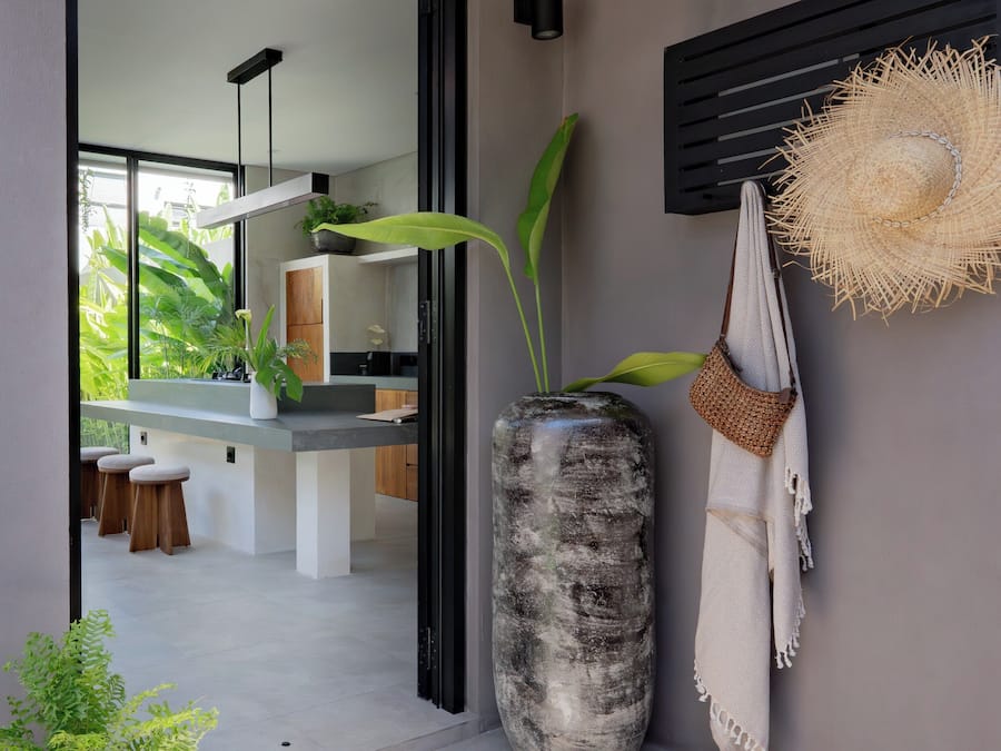 Una cocina moderna con una isla grande, un jarrón alto con una planta y un sombrero de paja colgado en la pared.