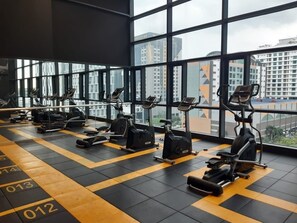 Un gimnasio con equipo de ejercicios y grandes ventanales que ofrecen vistas a la ciudad.
