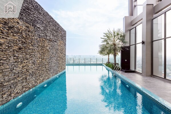 Une piscine à débordement située sur le toit, avec un mur en pierre et un bâtiment moderne en verre.