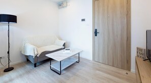 A room with a grey sofa, a white coffee table, a wooden wardrobe, and a television on a wooden stand. - 환상적인 짜오프라야 강 전망을 자랑하는 아늑한 고층 룸 (Chang Wat Nonthaburi)