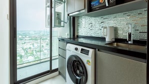A modern kitchen with a washing machine, a coffee maker, and a view of a cityscape through a large window.