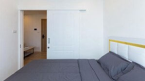 A bedroom with a bed, a door, and a bench in the adjacent room.